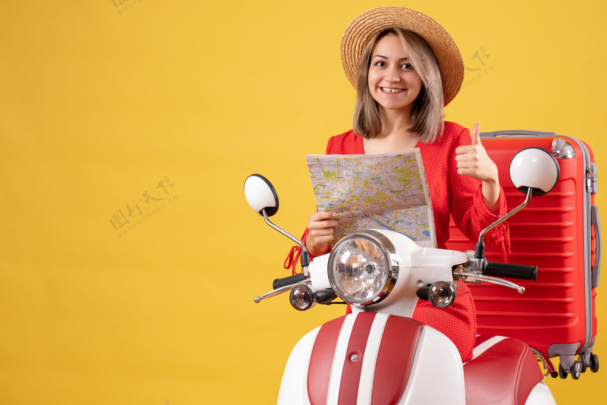 成人骑着轻便摩托车的漂亮女孩拿着红色手提箱举着地图竖起大拇指手提箱红色时尚