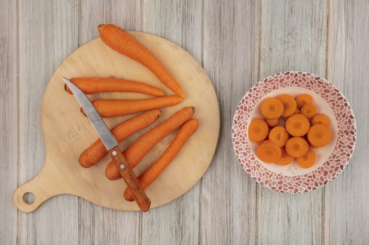 切碎顶视图橙色胡萝卜在一个木制的厨房板与切碎的胡萝卜在一个灰色的木制背景碗刀顶部蔬菜碗