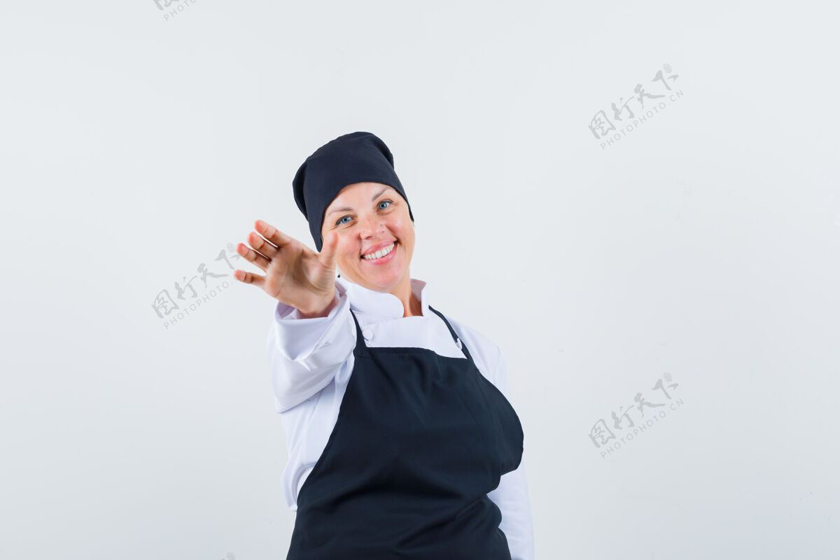健康身着黑色厨师制服的金发女人 双手伸向镜头 看起来很漂亮 正前方视图金发自然化妆