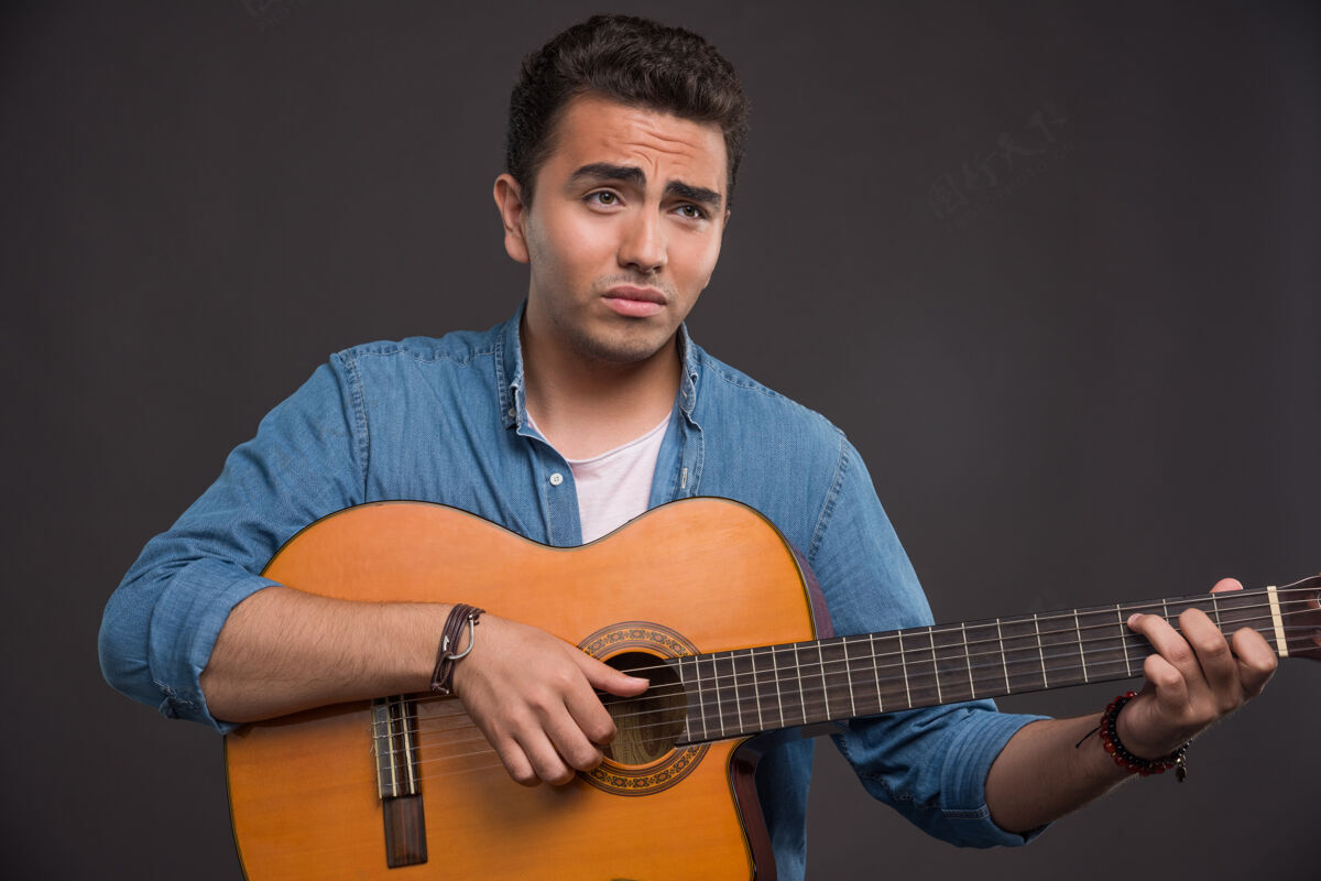 人在黑色背景下弹吉他的年轻音乐家男吉他和弦