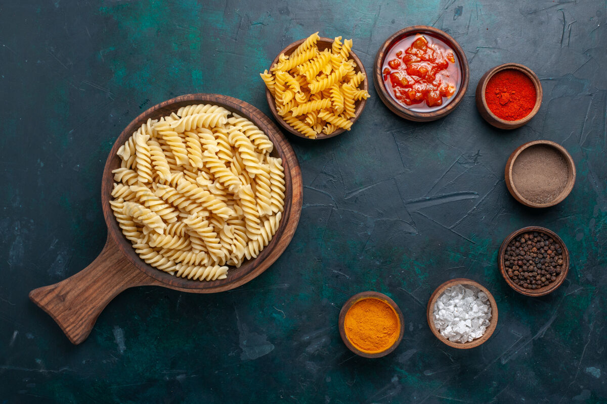 食物在深蓝色的桌子上 可以俯瞰形状各异的意大利面食 里面有酱汁和不同的调味品面食器具酱汁