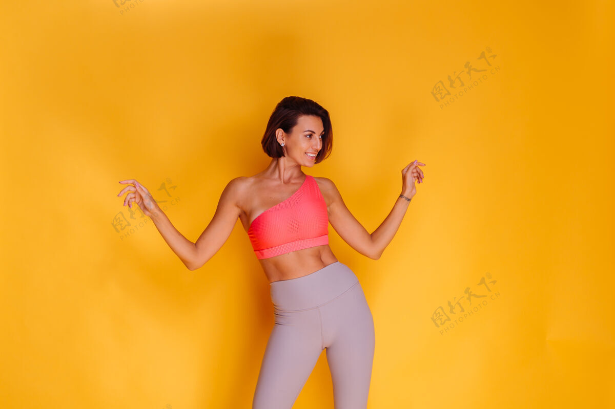 活跃年轻健壮的女人穿着运动服 时髦的上衣和紧身裤 对着黄色的墙壁摆姿势年轻服装运动