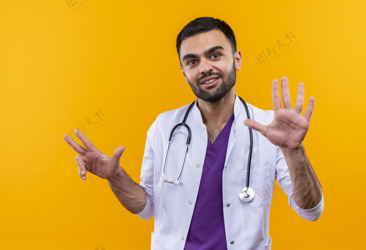 不同高兴的年轻男医生穿着听诊器医用长袍显示不同的数字与手孤立的黄色背景展示数字长袍