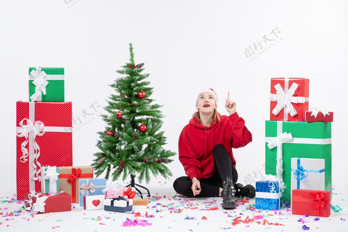 礼物年轻女子坐在白色墙壁上的节日礼物周围的正面视图节日灯人