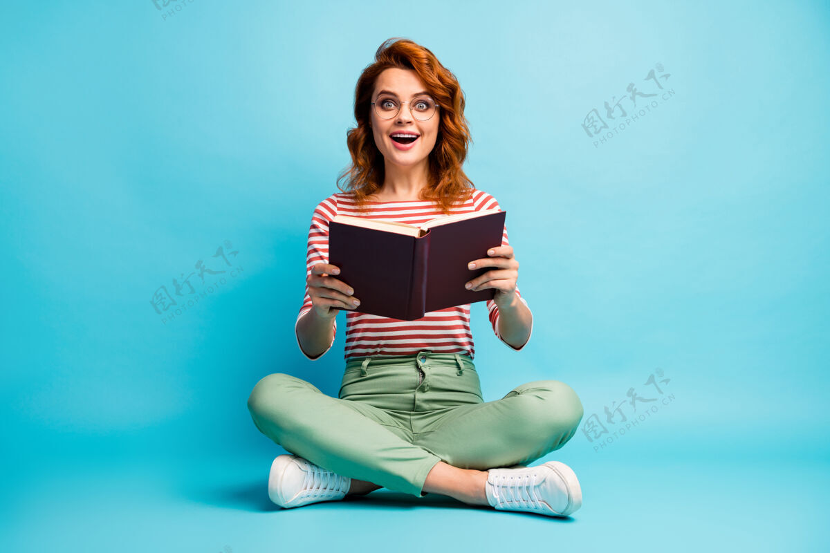 女学生兴奋的疯女人书呆子坐在地板上腿交叉阅读的故事印象深刻的书尖叫哇omg穿白色绿色裤子裤子蓝色隔离学习鞋微笑