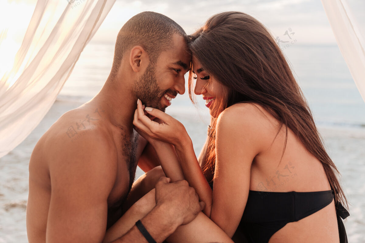 床微笑的年轻夫妇在沙滩上拥抱在床上太阳成人异国情调