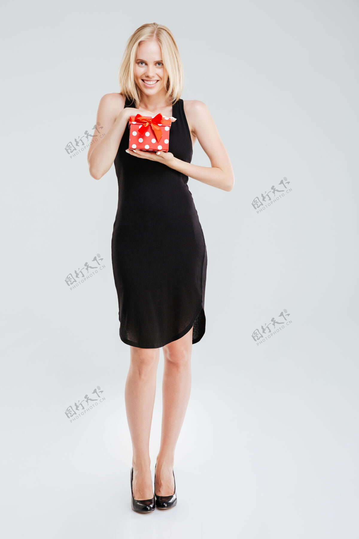 礼物在白色背景上 一位身着黑色连衣裙 手持礼物 面带微笑的女子的全长肖像礼物盒子女士