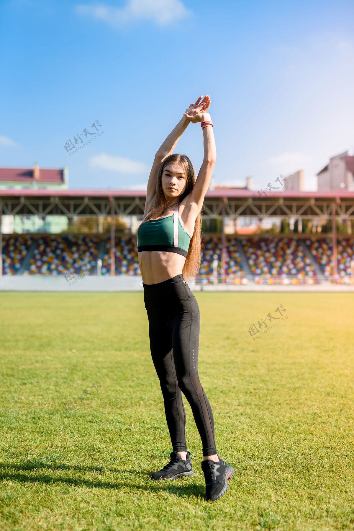 运动装漂亮的运动女孩在体育场草地上做体操夏季户外训练