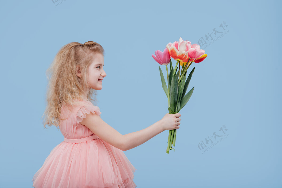 孩子小女孩穿着粉色连衣裙 手里拿着春花 孤零零地站在蓝色的墙上 侧视图侧面图赠送看