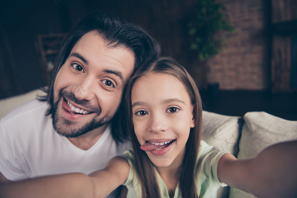年轻美丽可爱的小女孩和英俊年轻的爸爸坐在舒适的沙发上的照片拥抱在一起相机
