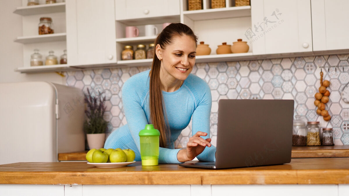 指向微笑的女人在现代厨房里使用电脑烹饪与健康生活理念一个女人正在寻找一个食谱或是在网上流微笑室内健康