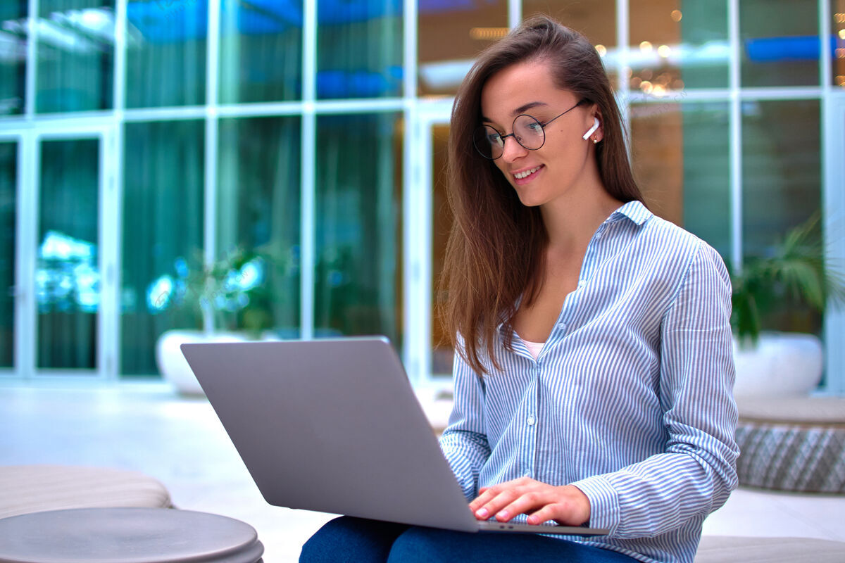 在线现代聪明的自由职业女性戴着无线耳机在电脑前远程在线工作生活方式工作计算机