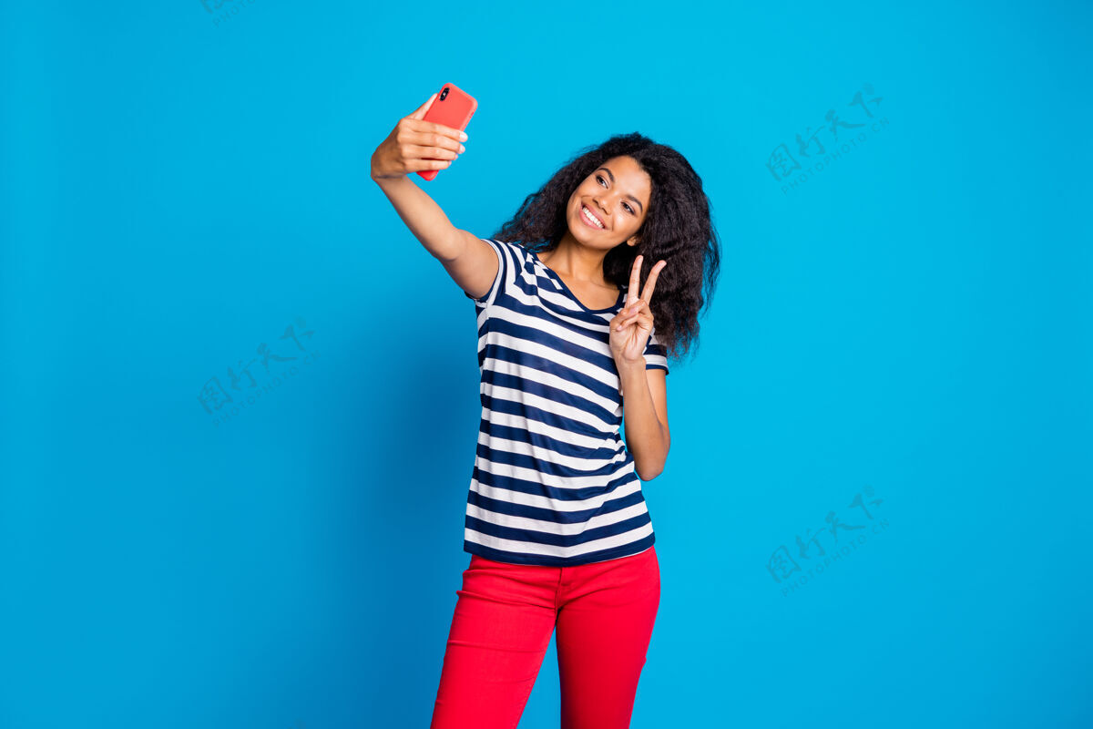 手指开朗可爱的好女人拿着手机自拍展示v字的照片和平电话手势