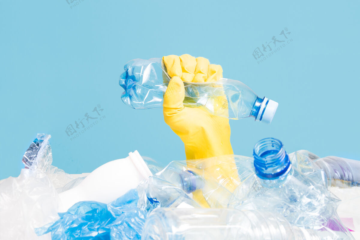 瓶一只手戴着橡胶手套挤压着一个皱巴巴的塑料瓶清洁回收产品