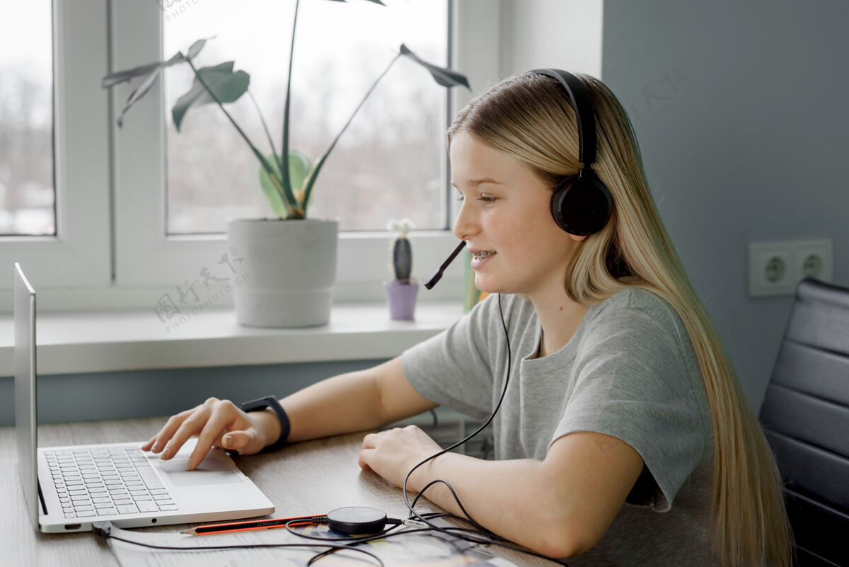 计算机戴着耳机微笑的少女在家里上网络课时使用笔记本电脑青少年课程远程