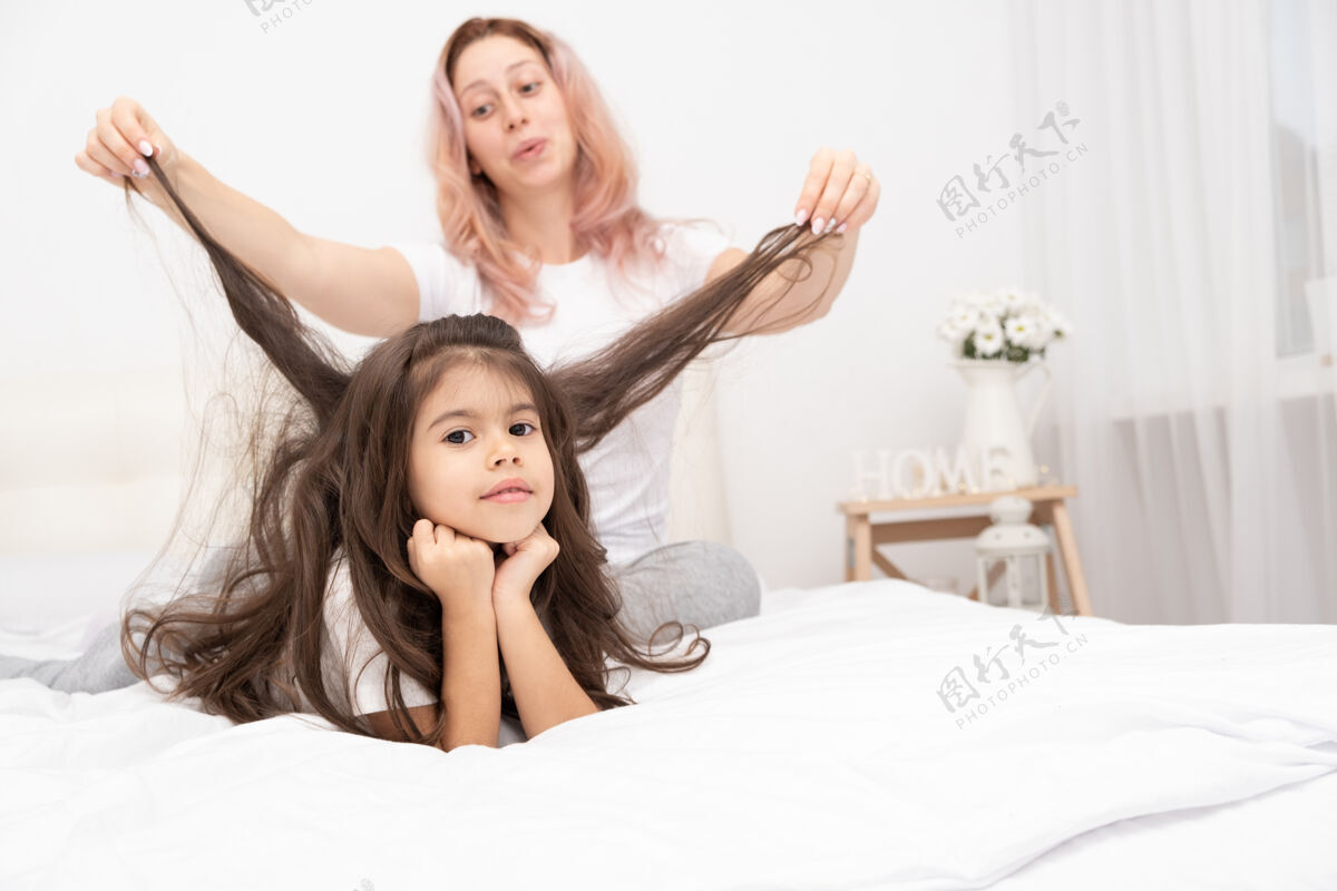 母女妈妈带着活泼的小女儿在家里的床上玩耍 玩得开心 和孩子们一起活动美丽休闲可爱的小信任关系