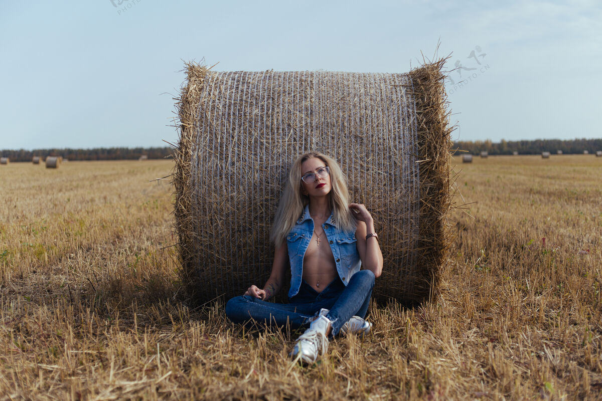 女人一位年轻漂亮的女村民穿着牛仔裤在一捆干草旁摆姿势姿势草包田野