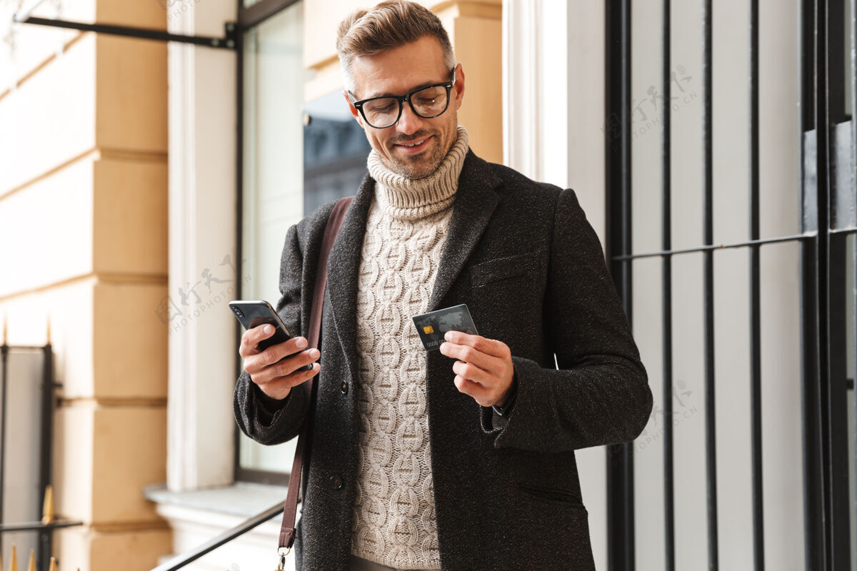 休闲帅哥穿着外套走在户外 用手机和信用卡在网上购物账单应用程序景点