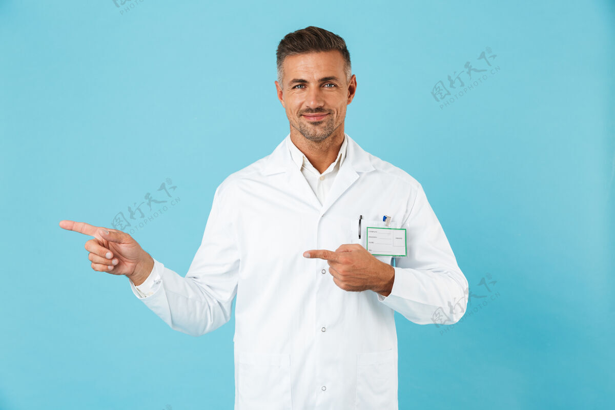 成人自信的男医生穿着制服孤立地站在蓝色的墙上 指着复印空间手指职业外科医生
