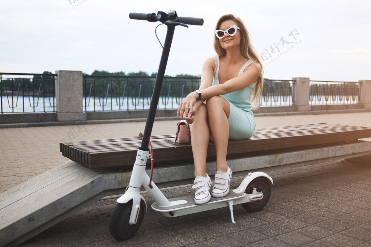 户外年轻时尚的女人在河边骑着电动滑板车长车辆时尚
