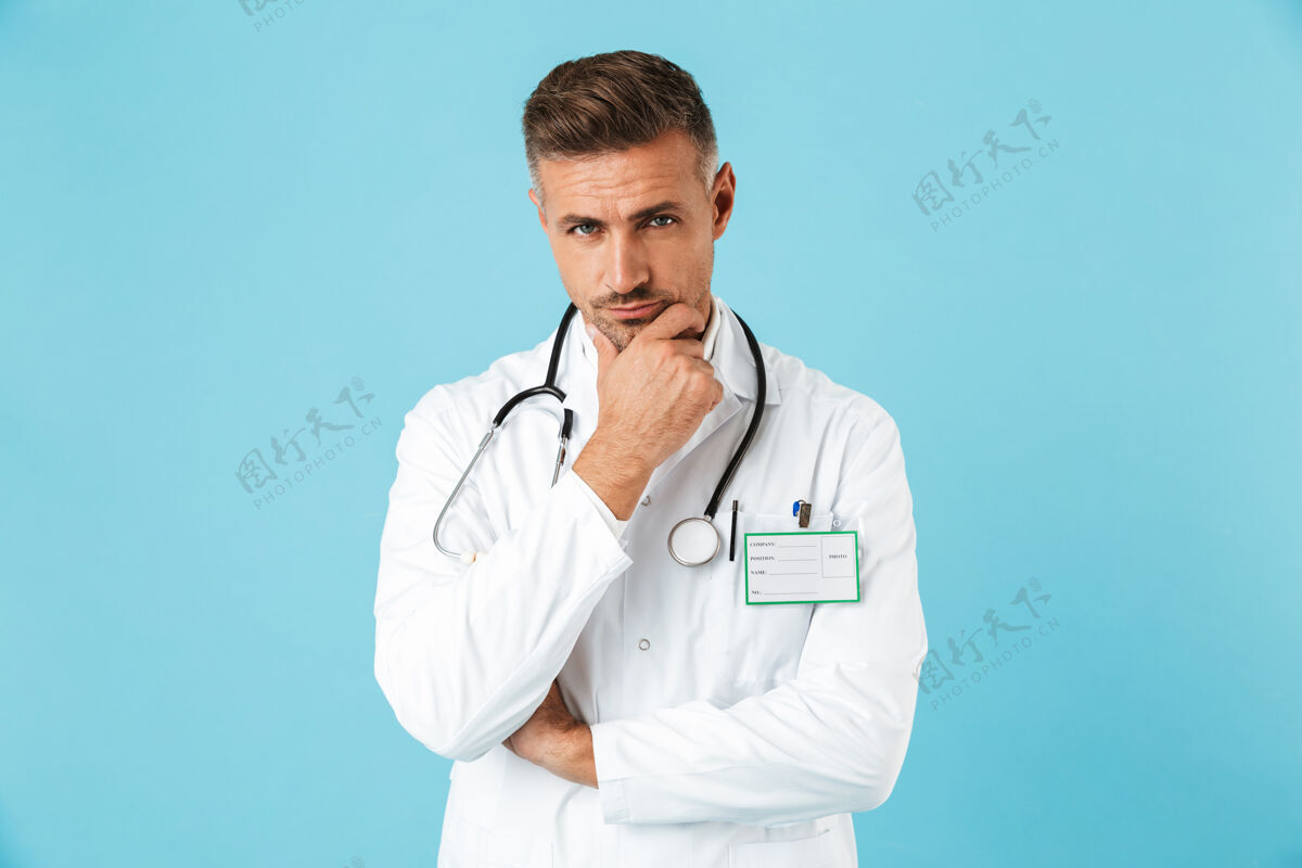 职业穿着白色制服 戴着听诊器的白人医生的画像 孤立地站在蓝色的墙上心脏病专家情绪中年