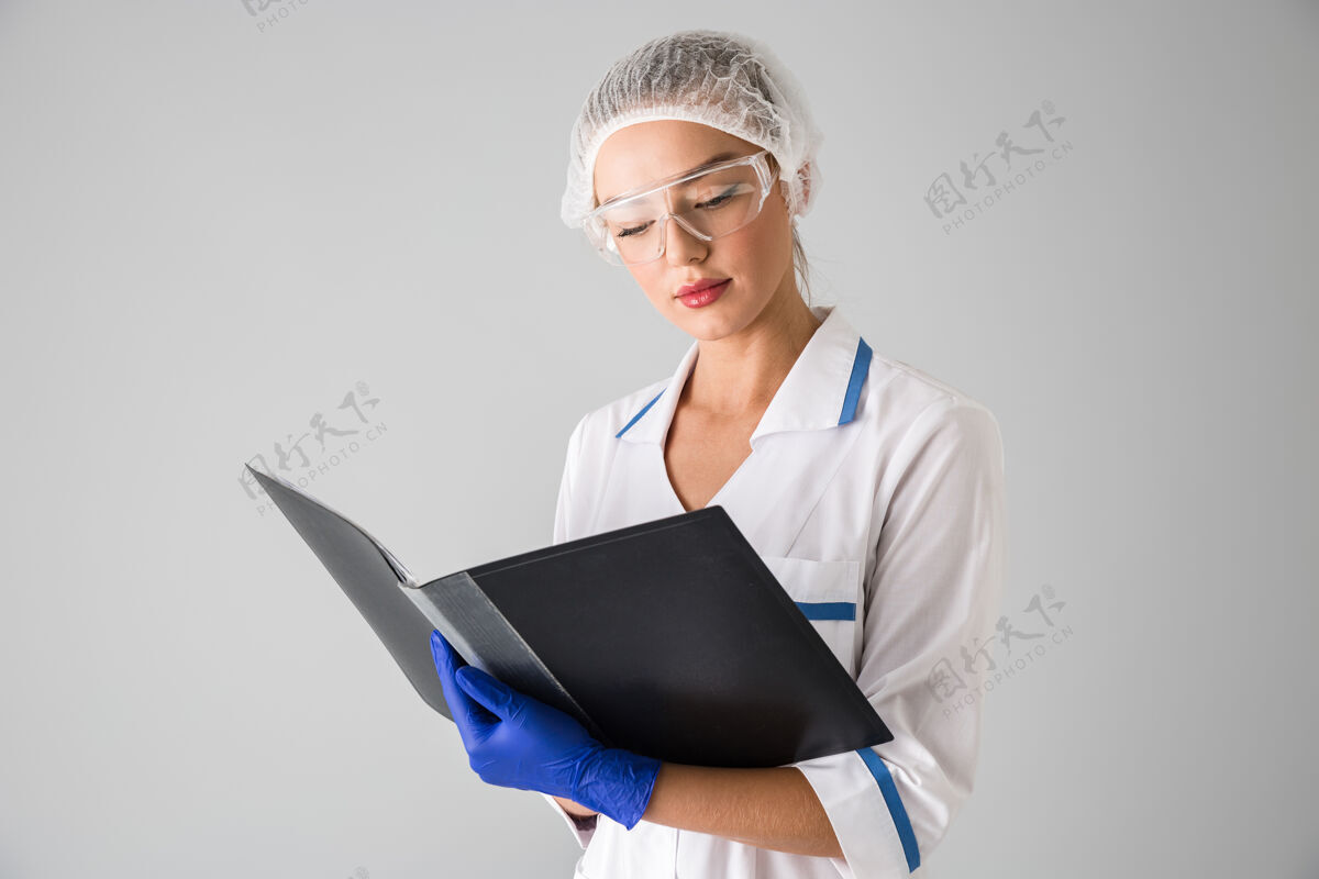 职业一个年轻漂亮的女美容师医生的形象被隔离在灰色的墙上拿着文件夹实践女人医生