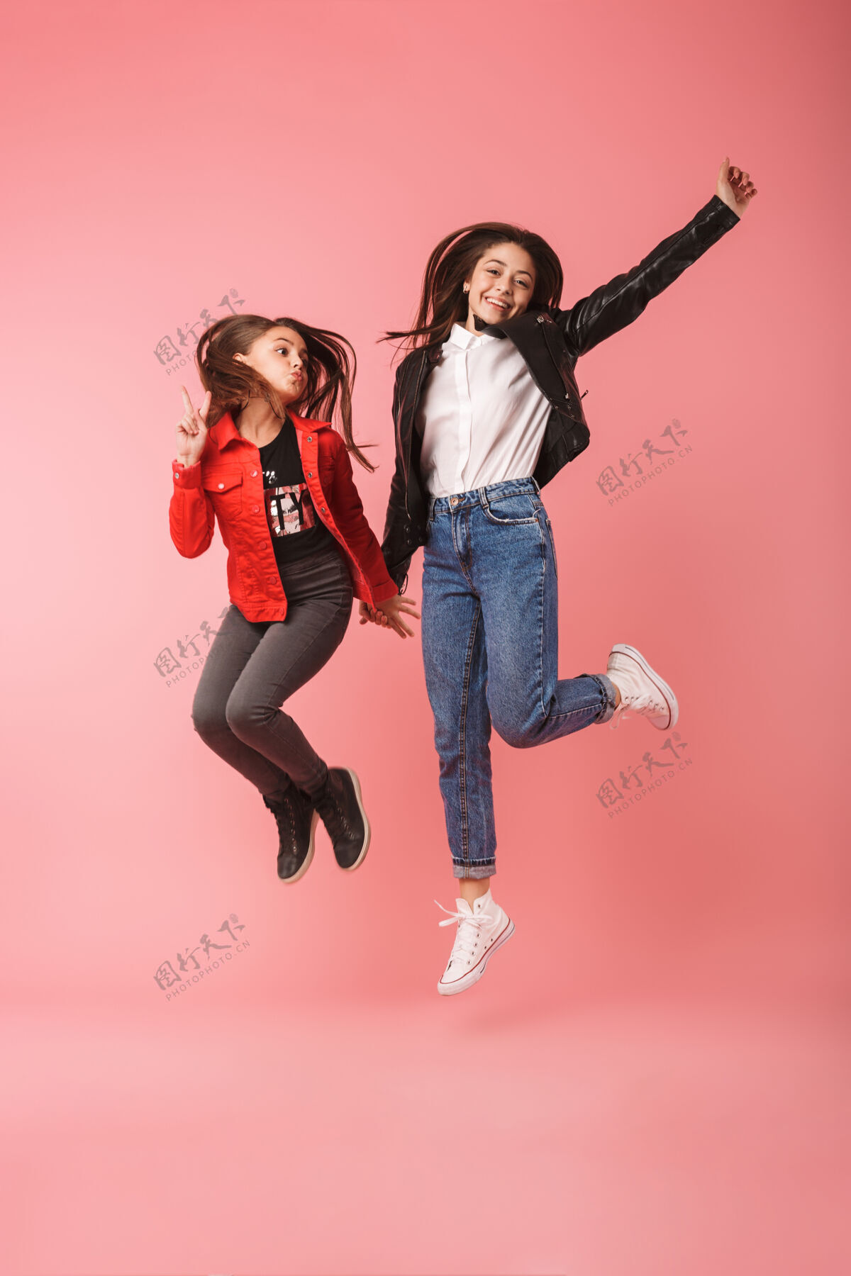 姐妹乐观的女孩在一起随意跳跃 隔着红墙孤立的全长照片跳跃完整奥本