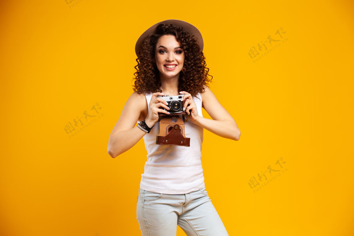 室内在明亮黄色的复古相机上拍摄的笑脸少女肖像黑发摄影师穿