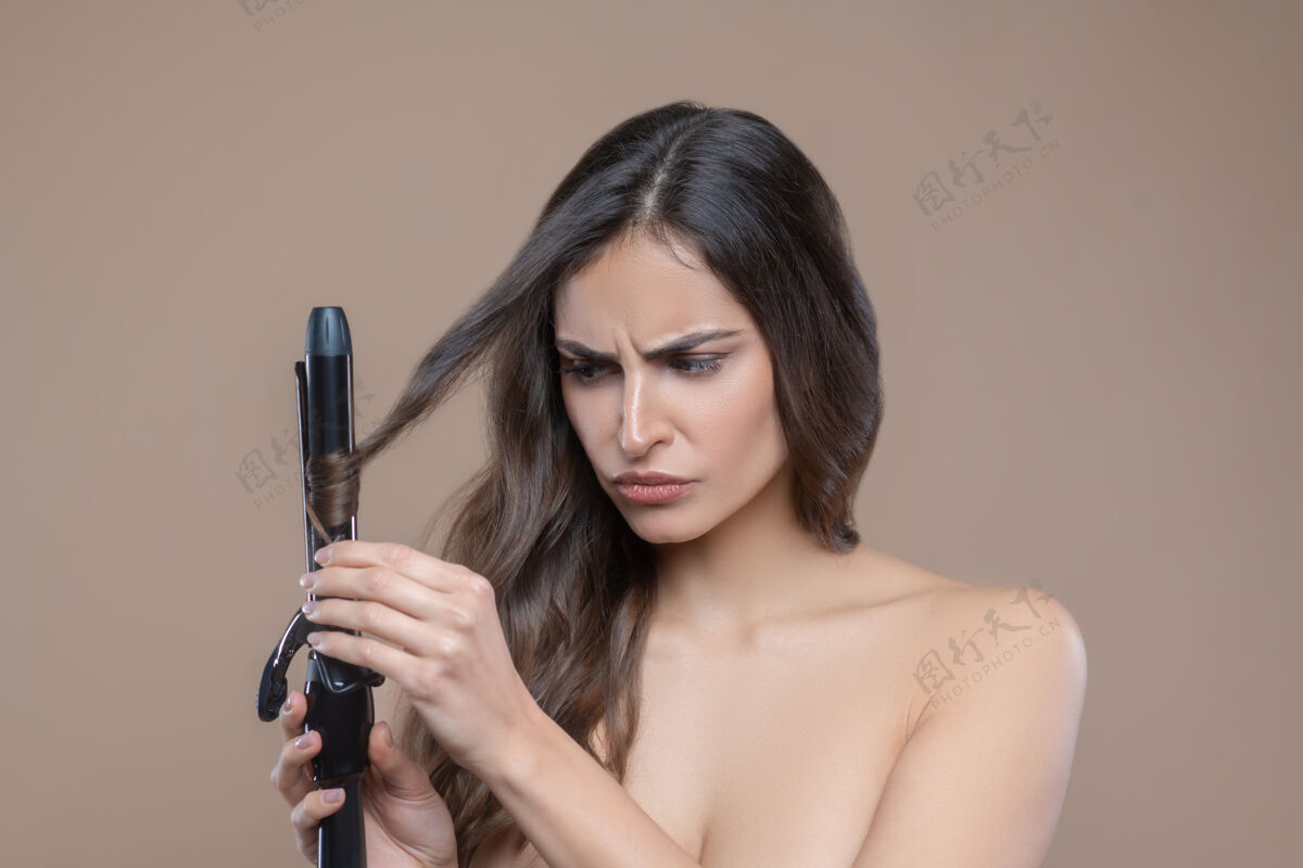 严格卷曲卷发认真的一个年轻的黑发女人 光着肩膀 用黑色卷发棒卷发裸体长发头发