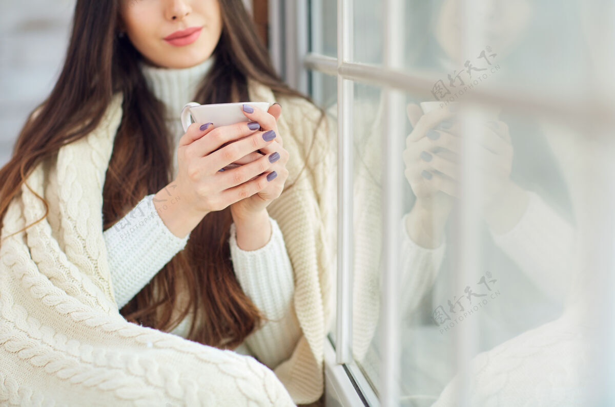 人冬天 女孩在窗前喝着一杯咖啡漂亮圣诞树坐着