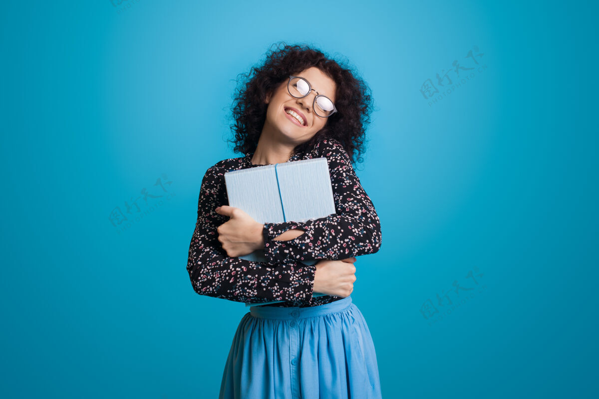 毛衣一位留着卷发 戴着眼镜的白种人 穿着裙子 抱着礼物盒微笑着站在蓝色工作室的墙上搞笑礼物高兴