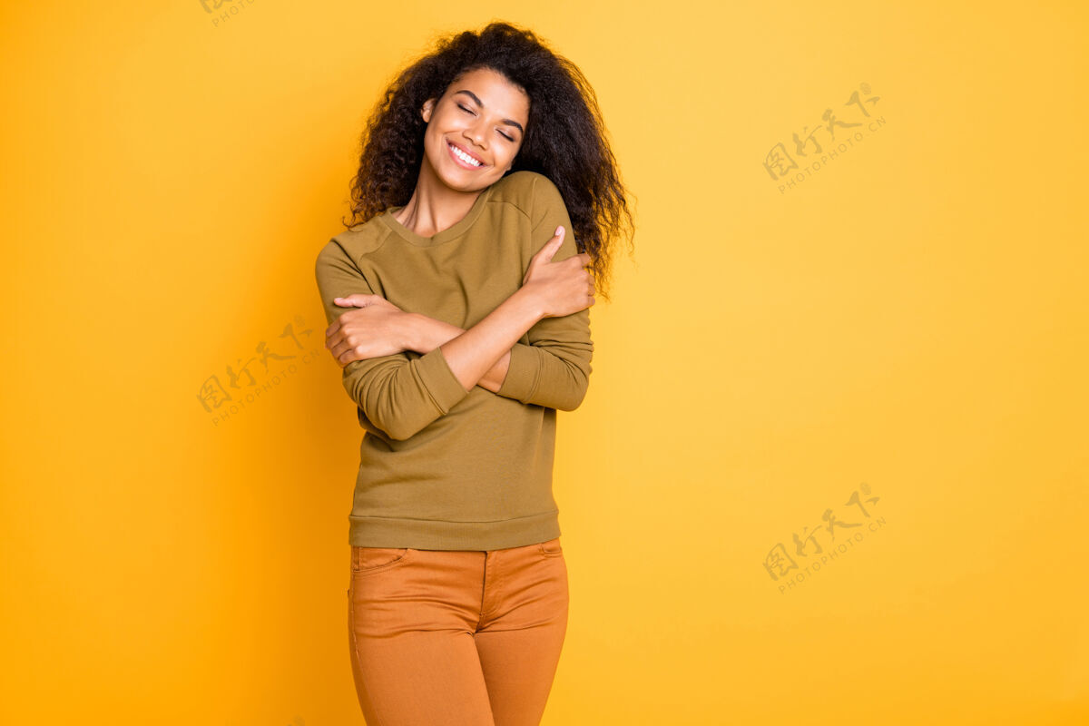 满足照片中欢快的牙齿微笑可爱迷人的黑人妇女穿着橙色裤子享受她的新买的毛衣在生动的色彩背景隔离放松女人皮肤
