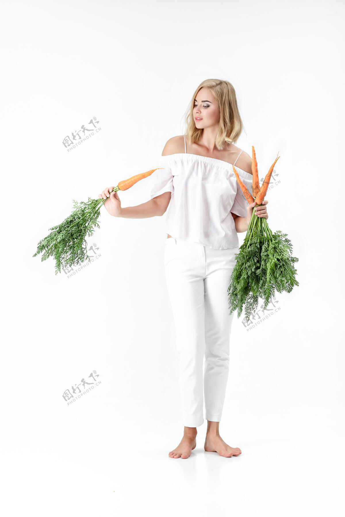 束一个穿着白衬衫的金发美女 手里拿着一根新鲜的胡萝卜 上面有绿叶背景.健康还有节食素食生活方式膳食