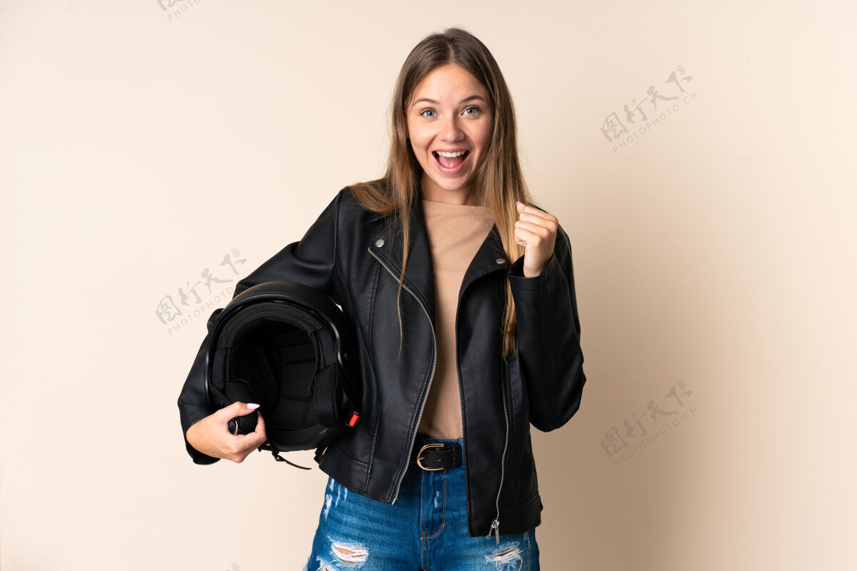 摩托车手立陶宛年轻女子手持摩托车头盔 背景为米色 庆祝胜利女人青年搞笑