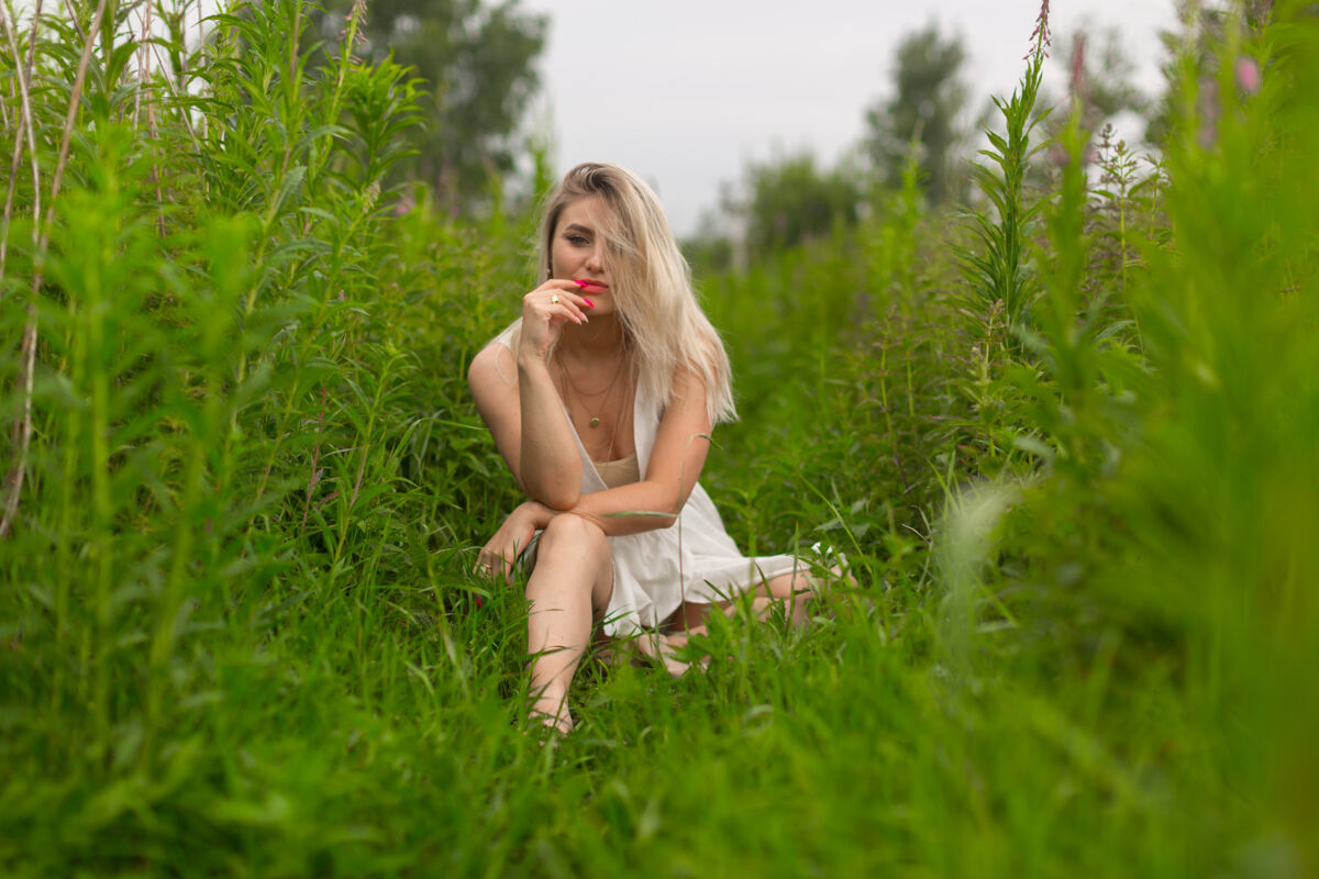 女人年轻的金发女郎带着红色唇膏和夏装 坐在绿草丛中女人 自然 女孩 草 衣服 户外 女性 年轻 美丽 肖像 坐着 成人 户外 姿势