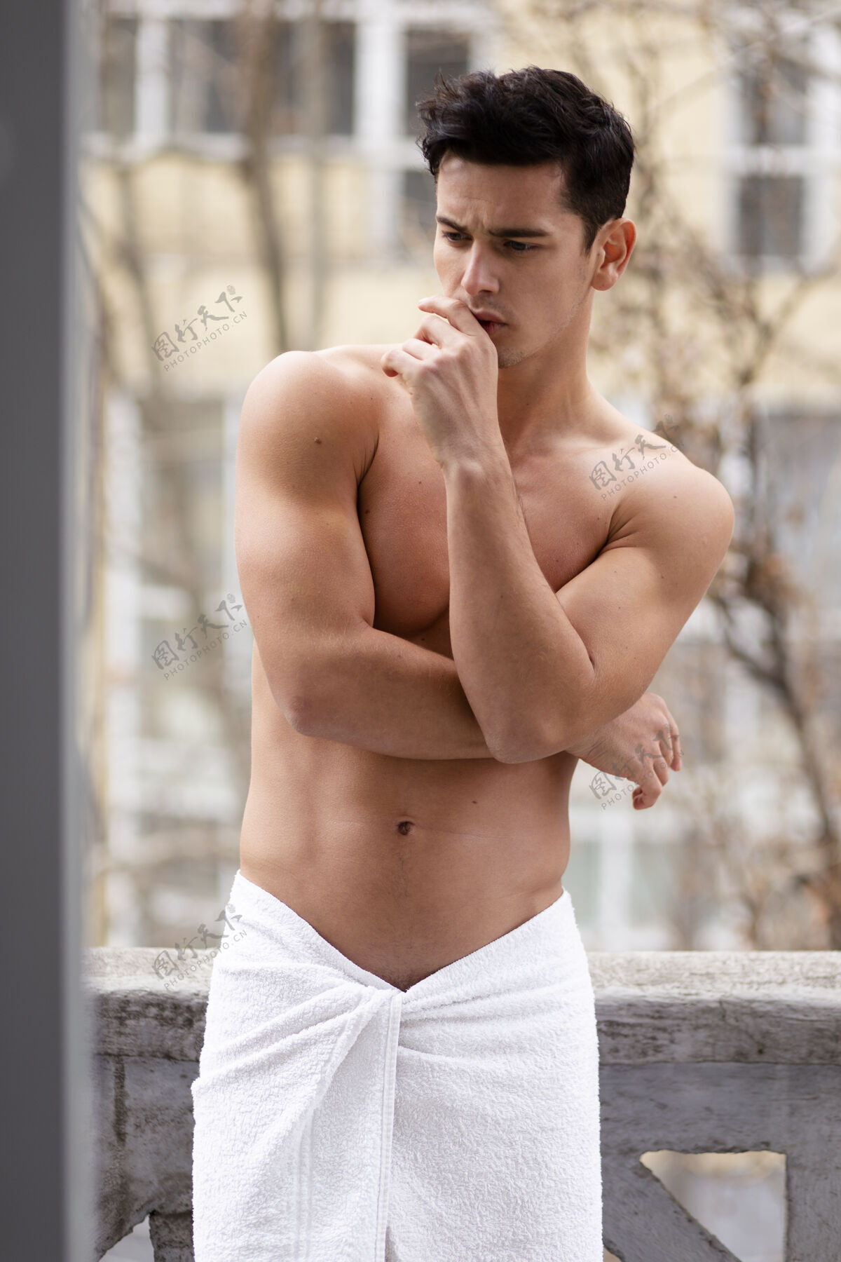 肌肉一个穿着浴巾 身材健美的运动型男人 站在阳台上 双手交叉 孤零零地站在街上背景.垂直查看运动员城市黑发