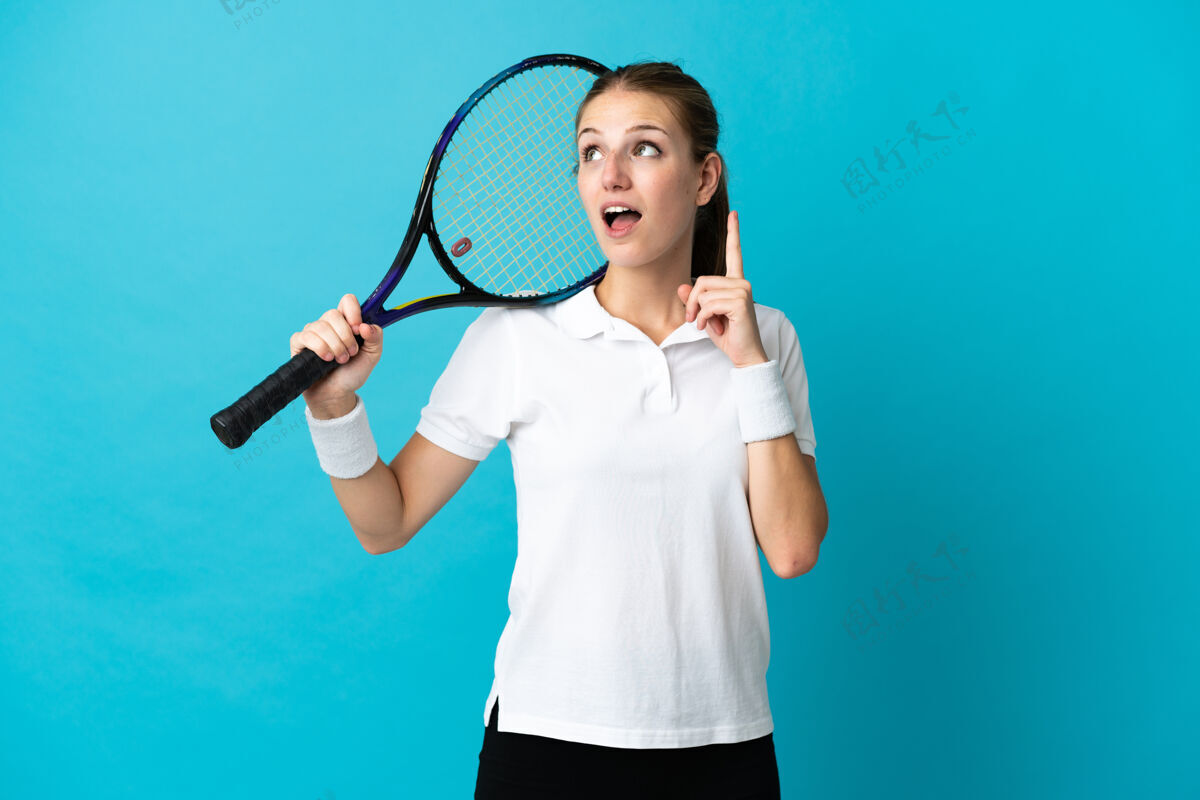 球拍年轻女子网球运动员孤立在蓝色背景下思考一个想法 手指向上游戏年轻看