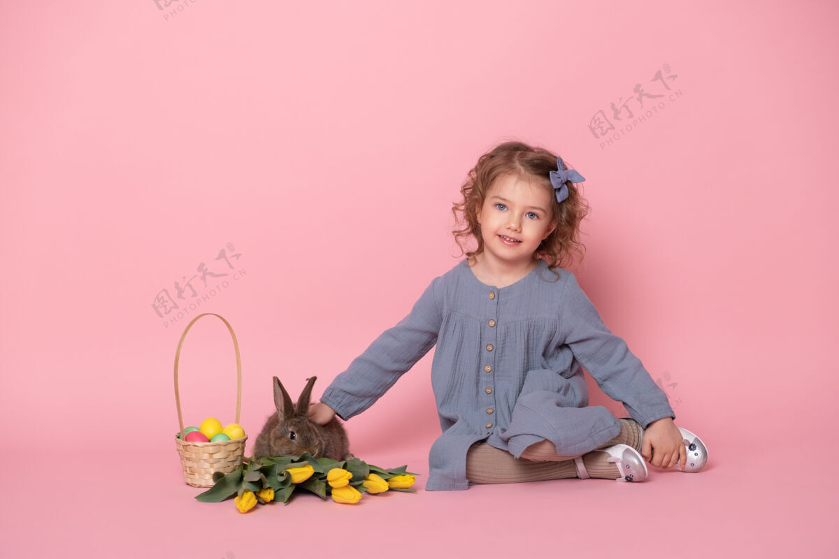 童年穿蓝色裙子的小女孩 带着兔子 郁金香 篮子里放着粉红色的彩蛋庆祝复活节传统