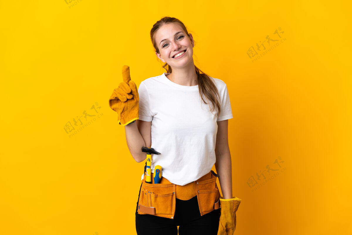 工艺在黄色背景上被隔离的年轻电工女士展示并举起手指示意最好木工年轻人职业