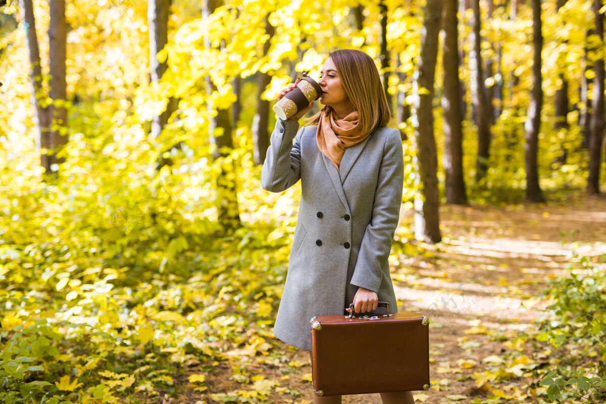 秋天秋天 自然 人的概念-年轻的黑发女人在秋天公园喝咖啡欢呼饮料户外