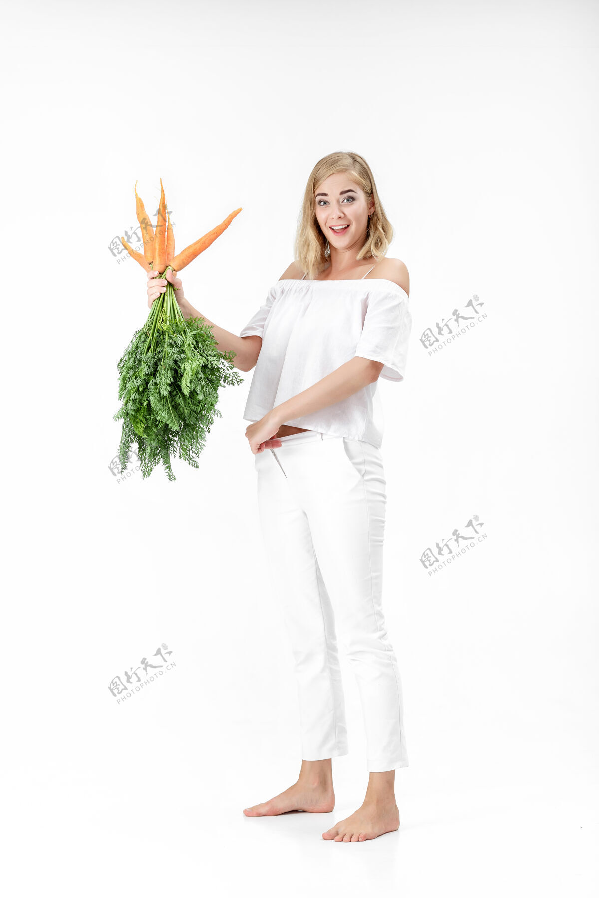 白色美丽的金发女人拿着一个新鲜的胡萝卜和绿色的叶子上的白色背景女孩吃胡萝卜会变瘦美丽吃可爱