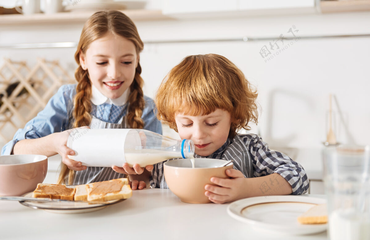 吃牛奶和巧克力明亮热情可爱的孩子 给她兄弟的谷类食品加点牛奶 让它尝起来像天堂一样美味围裙兄弟烹饪