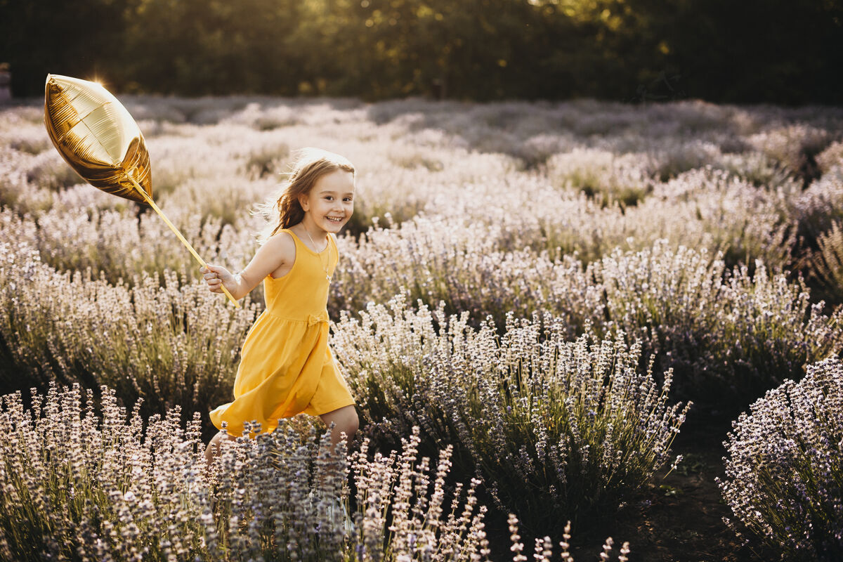 长可爱的小女孩看着相机微笑着拿着气球在花丛中奔跑自然波西米亚人