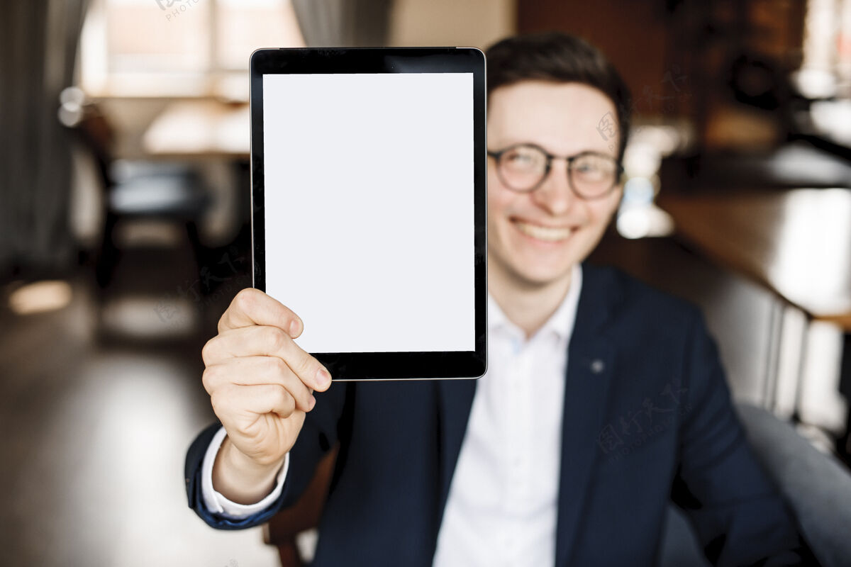 无线一个穿着西装的成年人坐在咖啡馆里 脸前拿着一块平板电脑 脸上露出微笑成人办公室公司