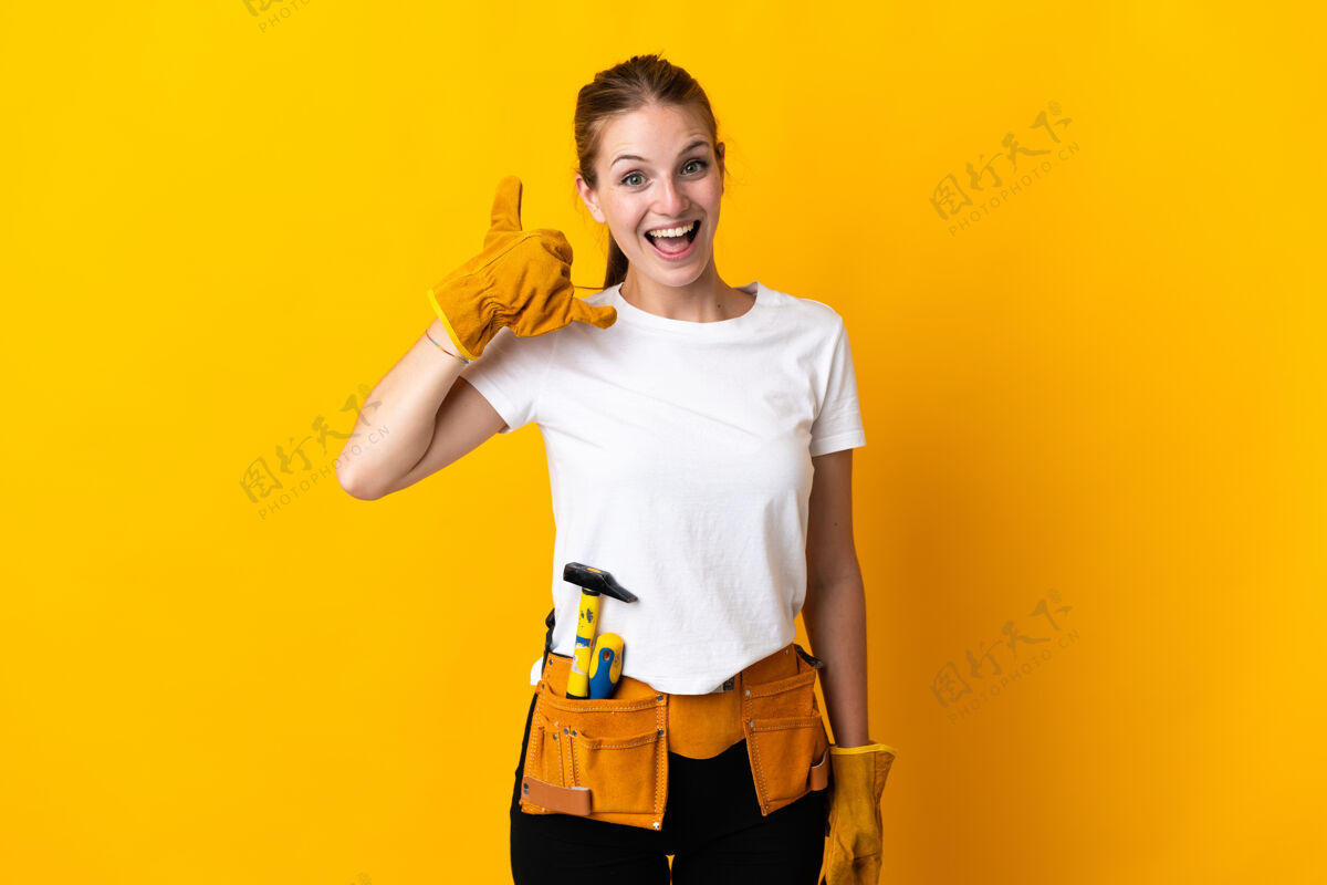 木工被隔离在黄色背景手机上的年轻女电工手势.呼叫给我回个手势年轻手势女人