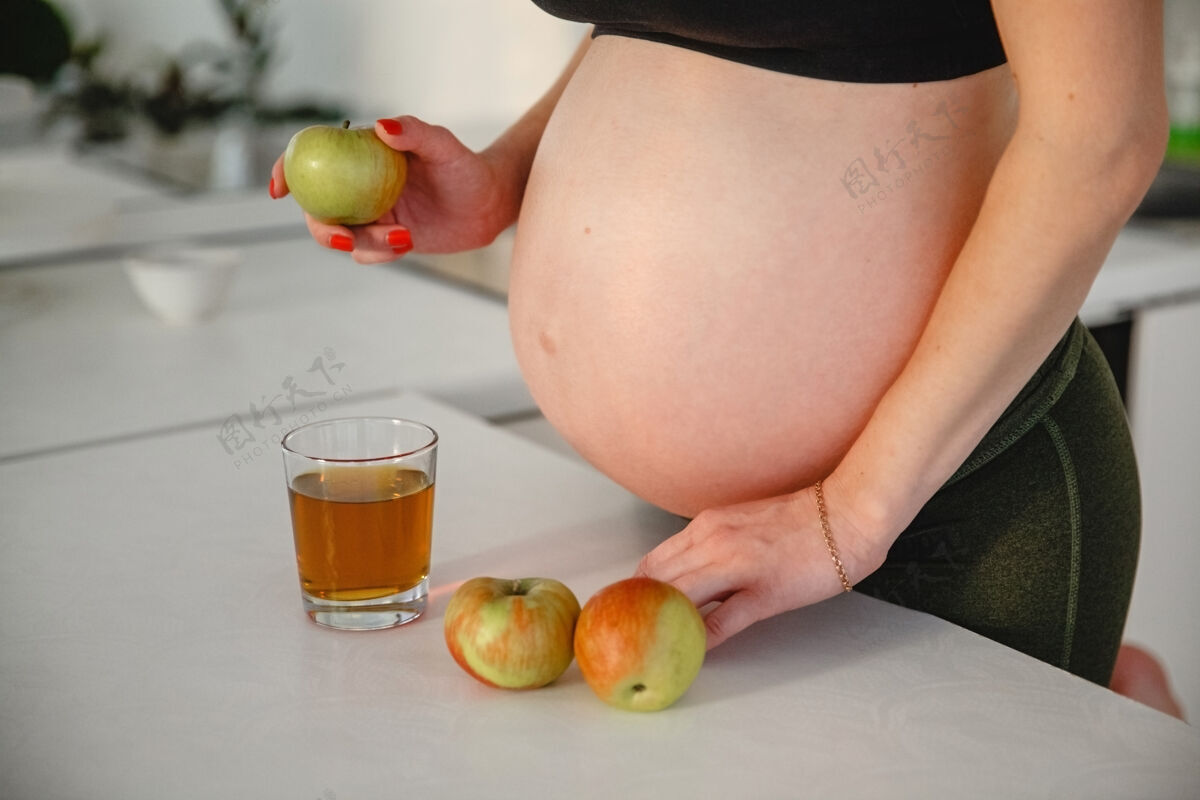 杯子一个光着肚子的孕妇站在桌子旁边 手里拿着苹果手靠近是一杯苹果汁水果生活零件