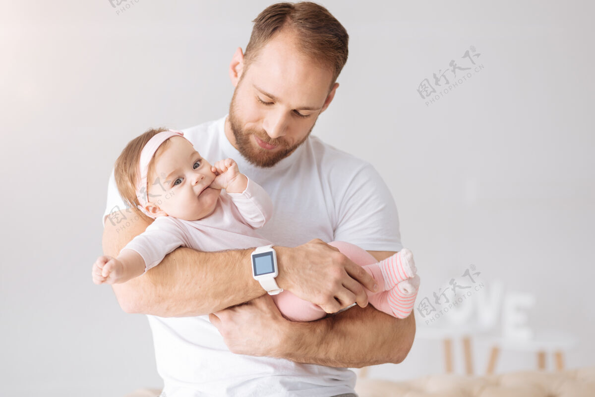 爸爸快乐周末迷人可爱漂亮的女婴躺在爸爸的手里 一边看着别处 一边表达着兴趣和喜悦后代父母传统