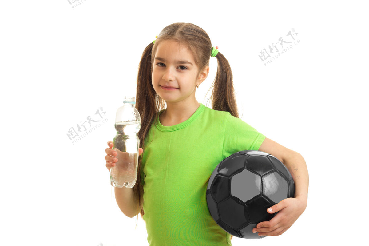 肖像可爱的小女人手里拿着足球 在白色的瓶子里喝水可爱人球迷