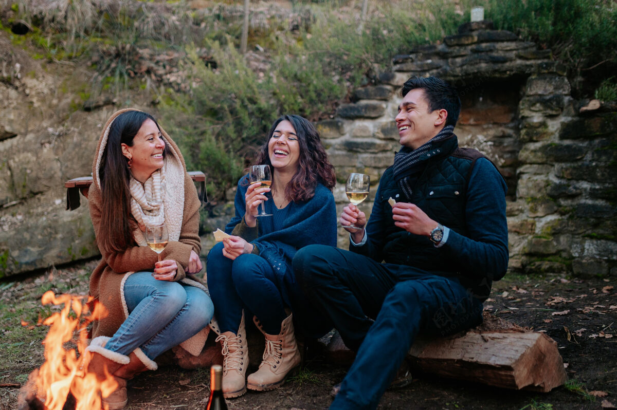 家庭一群朋友坐在篝火前一边喝酒一边聊天欢笑团结友谊的概念分享森林食物