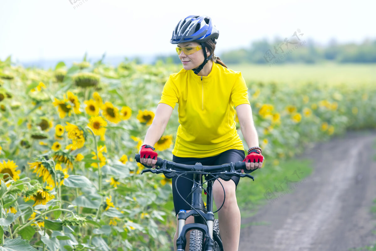 场地骑自行车的美女骑着向日葵在草地上自行车健康生活方式和运动休闲和爱好头盔健康自行车手